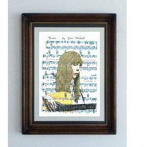May include: Framed art print featuring a drawing of a person playing a yellow guitar, with long blonde hair, set against a backdrop of sheet music. The text "River by Joni Mitchell" is visible at the top. The frame is dark brown.