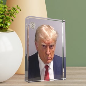 May include: A close-up portrait of a man with blonde hair wearing a dark blue suit and a red tie. He has a serious expression on his face.