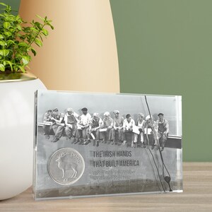 May include: A clear acrylic block with a black and white photo of a group of men sitting on a beam. The photo is captioned "The Irish Hands That Built America" and "Lunch Atop a Skyscraper, September 20th, 1932". A silver coin with a deer design is in the lower left corner.