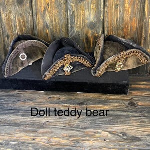 May include: Three antique doll hats in shades of brown and black, displayed on a black surface. The hats feature decorative trim and embellishments, with the text "Doll teddy bear" at the bottom.