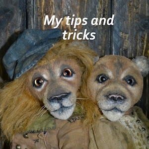 Peut inclure: Deux jouets en peluche faits à la main, un lion portant une casquette bleue et un chien brun, tous deux avec des traits réalistes et un tissu vieilli. Le lion porte une veste brune avec des boutons dorés et une clé. Le chien porte une robe brune avec une bordure en dentelle blanche. L'arrière-plan est une surface en bois avec le texte "Mes conseils et astuces".