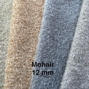 Op de afbeelding: Close-up van mohair stofstalen in verschillende kleuren: lichtbeige, bruin, lichtblauw en grijs. De tekst "Mohair 12 mm" is zichtbaar. De stof heeft een zachte, donzige textuur.