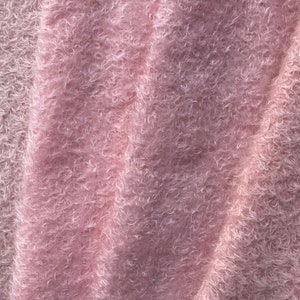 May include: Close-up of a soft, pink, fuzzy fabric with a textured surface. The fabric is folded and draped, creating a soft, luxurious look.