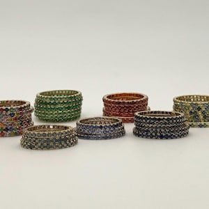 Puede incluir: Un conjunto de ocho anillos apilables con piedras preciosas de colores. Los anillos son de oro y presentan una variedad de colores, incluyendo verde, rojo, azul y blanco.