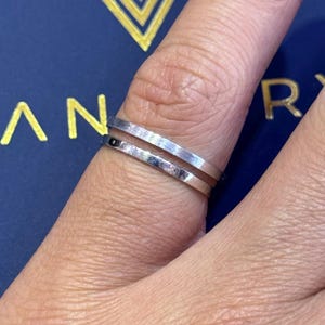 May include: Two silver rings worn on a finger. The rings are thin and have a smooth, polished finish.