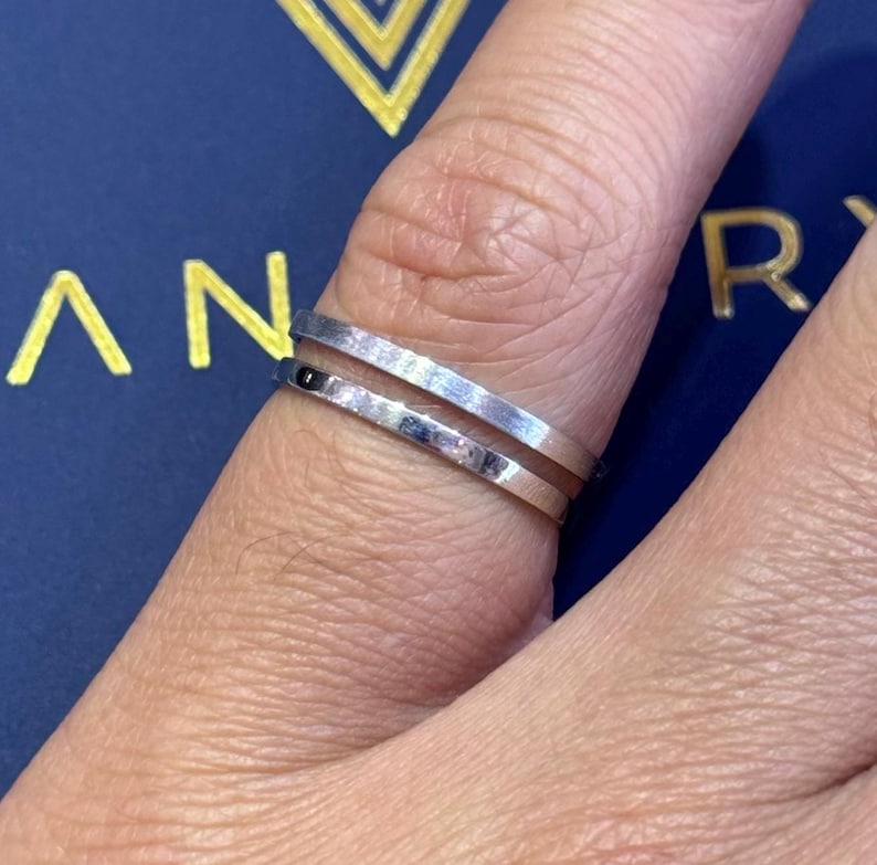 May include: Two silver rings worn on a finger. The rings are thin and have a smooth, polished finish.