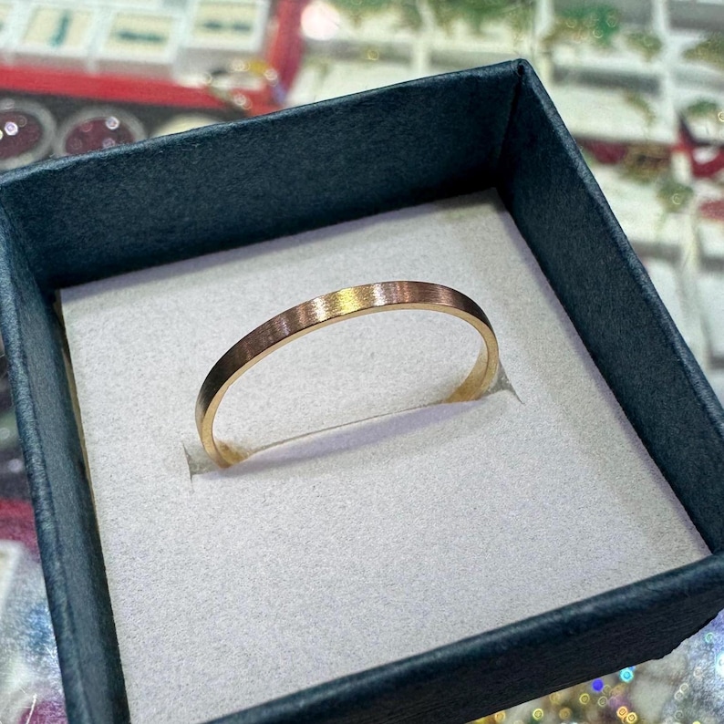 May include: A simple gold band ring in a white velvet ring box. The ring is smooth and has a brushed finish.
