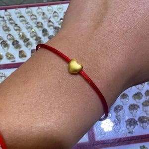 Pode incluir: Uma pulseira de cord&atilde;o vermelho com um pequeno berloque de cora&ccedil;&atilde;o dourado. A pulseira tem um design simples, com o berloque de cora&ccedil;&atilde;o posicionado no centro do cord&atilde;o. O cora&ccedil;&atilde;o dourado tem um acabamento liso e polido.