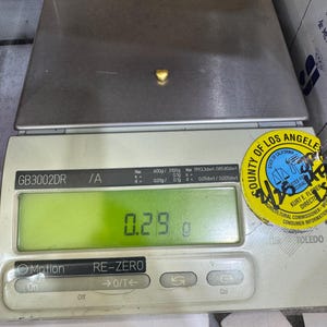 Pode incluir: Um pequeno objeto dourado em forma de cora&ccedil;&atilde;o est&aacute; sobre uma balan&ccedil;a digital. A balan&ccedil;a mostra uma leitura de 0,29 g. A balan&ccedil;a tem um visor digital verde e um adesivo do Condado de Los Angeles.