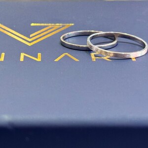 May include: Two silver wedding bands, one slightly larger than the other, are displayed on a blue box with the word "ANNARI" in gold lettering.