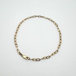 May include: A gold-colored chain bracelet with an oval link design. The bracelet is displayed on a white background. The clasp is visible and is also gold-colored. The bracelet is a delicate piece of jewelry.