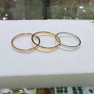 Könnte beinhalten: Drei verbundene Ringe in Roségold, Gold und Silber. Die Ringe sind dünne Bänder, jeweils mit einer glatten, polierten Oberfläche. Die Ringe werden auf einer weißen Oberfläche präsentiert.