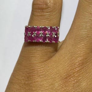 May include: A silver ring with a double row of pink oval-shaped gemstones. The ring is on a finger.