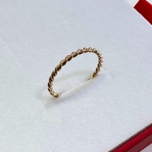May include: A thin gold band ring with a twisted rope design.
