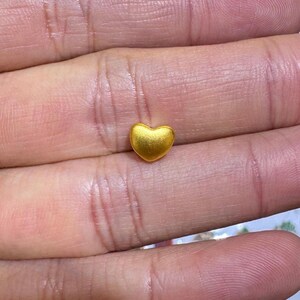 Pode incluir: Um pequeno pingente em forma de cora&ccedil;&atilde;o dourado. O pingente tem uma superf&iacute;cie lisa e polida e &eacute; colocado sobre um fundo de pele. O cora&ccedil;&atilde;o &eacute; um s&iacute;mbolo de amor e carinho.
