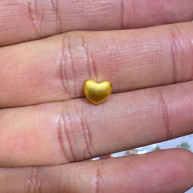 Pode incluir: Um pequeno pingente em forma de cora&ccedil;&atilde;o dourado. O pingente tem uma superf&iacute;cie lisa e polida e &eacute; colocado sobre um fundo de pele. O cora&ccedil;&atilde;o &eacute; um s&iacute;mbolo de amor e carinho.