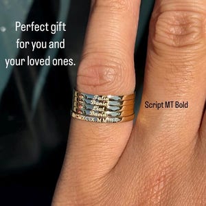 May include: A set of four gold stacking rings with the names Talia, Daniel, Liai, and David engraved on them. The rings are stacked on a finger and the font is Script MT Bold.