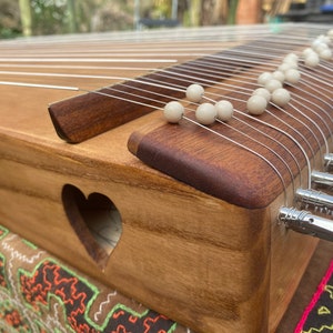 Peut inclure: Un instrument de musique en bois avec des cordes et des perles blanches. L'instrument a une découpe en forme de cœur sur le côté.