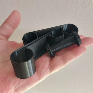 May include: A black plastic 3D printed object with three circular openings. The object is designed to hold multiple items, such as pens or pencils.