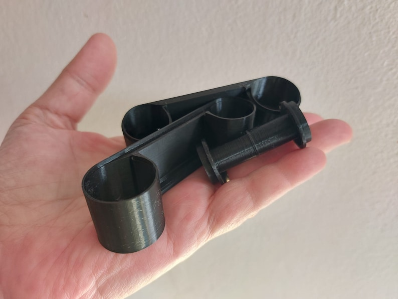 May include: A black plastic 3D printed object with three circular openings. The object is designed to hold multiple items, such as pens or pencils.