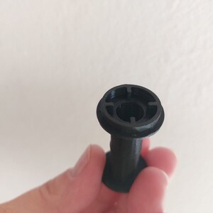 May include: A black plastic spool with a circular opening in the center. The opening has a small, circular hole in the center.