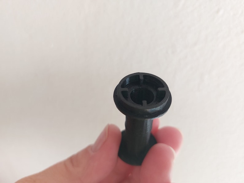 May include: A black plastic spool with a circular opening in the center. The opening has a small, circular hole in the center.