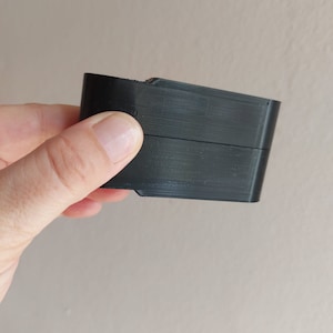 May include: A black plastic object with a rectangular shape and a slight curve on one side.