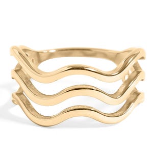 May include: A gold ring featuring three parallel, wavy bands that are connected at the sides. The metal has a polished, reflective finish, creating a smooth and continuous undulating design that wraps around the finger in a layered, open structure.