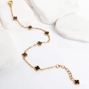 Gold Small Floral Motif Bracelet  with black flower-shaped charms on a white surface