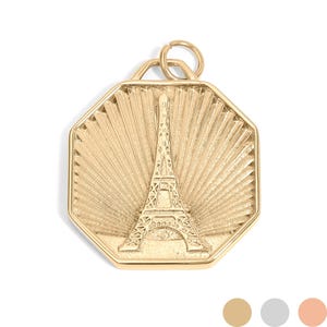 Può includere: Ciondolo dorato con la Torre Eiffel. Il ciondolo ha una forma ottagonale con un motivo a raggi di sole dietro la torre. Un piccolo anello nella parte superiore per una catena. Gioiello.