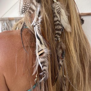 May include: Bohemian-style hair accessory featuring a headband with attached feathers in shades of brown, gray, and white. The feathers are accented with delicate metal and bead details, creating a natural and earthy aesthetic. Perfect for festivals or everyday wear.