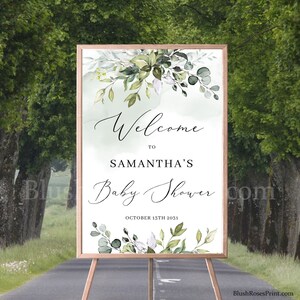 May include: Welcome to Samantha's Baby Shower sign with a green and white floral design. The sign is on a wooden easel and has the date October 15th 2031.