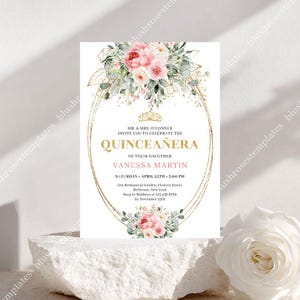 May include: A Quinceañera invitation with a floral design. The invitation features a gold oval frame with text in gold and pink, including the name "Vanessa Martin" and event details. Floral arrangements with pink roses and greenery adorn the top and bottom.