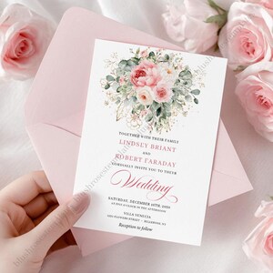 May include: A wedding invitation with a floral design featuring pink and white roses, green leaves, and gold accents. The invitation is held in a pink envelope. The text reads "Lindsey Briant and Robert Faraday" and "Wedding".