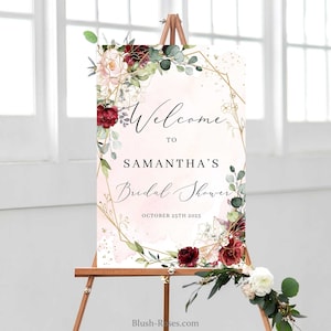 Op de afbeelding: Een welkomstbord voor een bruidsdouche met een roze en gouden geometrisch frame, bordeauxrode en roze bloemen en groen. De tekst luidt "Welkom bij Samantha's Bridal Shower op 25 oktober 2025".