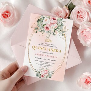 May include: A quinceañera invitation with a pink and gold design. The invitation features floral arrangements and the text "Quinceañera" in gold lettering. The invitation is held in a pink envelope, with pink roses in the background.