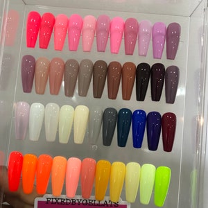 Puede incluir: Una colección de uñas postizas en varios colores, incluyendo tonos de rosa, morado, marrón, blanco, gris, azul y neón. Las uñas están dispuestas en filas, mostrando una gama de tonos y acabados. El texto "FIXEDBYGELLATS" es visible en la parte inferior.