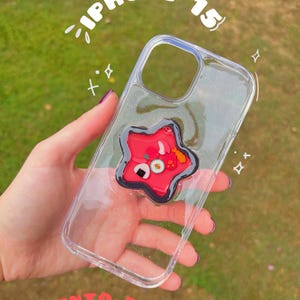 May include: Clear iPhone 15 case with a red star-shaped bento box design. The case has glitter accents and the text "iPhone 15" and "Bento Box Shaker".