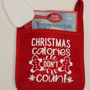 May include: Red oven mitt with the text "Christmas calories don't count" and two gingerbread men. A white Betty Crocker Sugar Cookie mix box is in the pocket of the oven mitt.