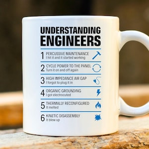 May include: White ceramic mug with the text "UNDERSTANDING ENGINEERS" in black. Below the title are six numbered engineering troubleshooting steps with accompanying blue icons. The mug has a curved handle.