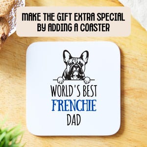 Op de afbeelding: Witte keramische onderzetter met een zwart-witte illustratie van een Franse Bulldog die over de rand kijkt. De tekst "World's Best Frenchie Dad" is in zwart en blauw gedrukt.