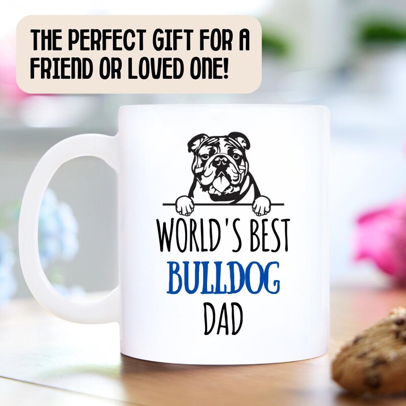 May include: White ceramic mug with a black and white illustration of a bulldog peeking over the rim. The text "World's Best Bulldog Dad" is printed in blue on the mug.