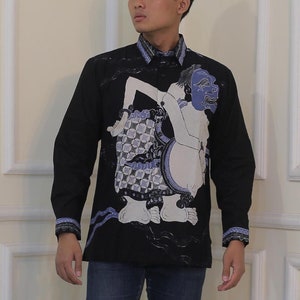 Puede incluir: Una camisa negra de manga larga con un diseño estampado en azul y blanco que presenta un motivo tradicional indonesio. La camisa se lleva con jeans azul oscuro y zapatillas blancas.