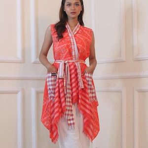 May include: A red and white patterned sleeveless top with a sash and pockets. The top has a V-neck and a flowing, asymmetrical hemline.