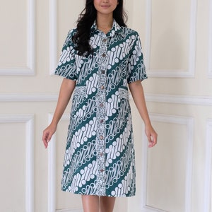 May include: A green and white patterned dress with short sleeves and a button-down front. The dress features a unique batik design and is knee-length. The model is wearing black platform heels.