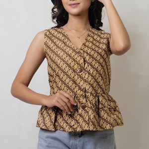 May include: A sleeveless brown and yellow patterned blouse with a ruffled hem and a button-up front. The blouse has a V-neckline and is worn with a gold necklace.