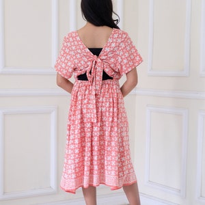 Puede incluir: Un vestido midi rosa coral con estampado floral blanco. El vestido tiene la espalda atada y mangas cortas.
