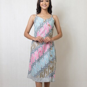 Puede incluir: Una mujer con un vestido estampado en gris, azul y rosa con botones en el lateral. Lleva tacones negros.