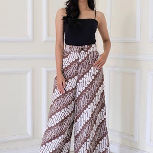 以下が含まれることがあります： 黒いタンクトップと白と茶色の模様のワイドレッグパンツを履いた女性。パンツは白地に茶色の丸と線の模様が入っている。