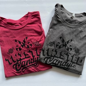May include: Two t-shirts with a black and white graphic design of candy canes and the text "Twisted Candy Co.". The t-shirts are red and gray.